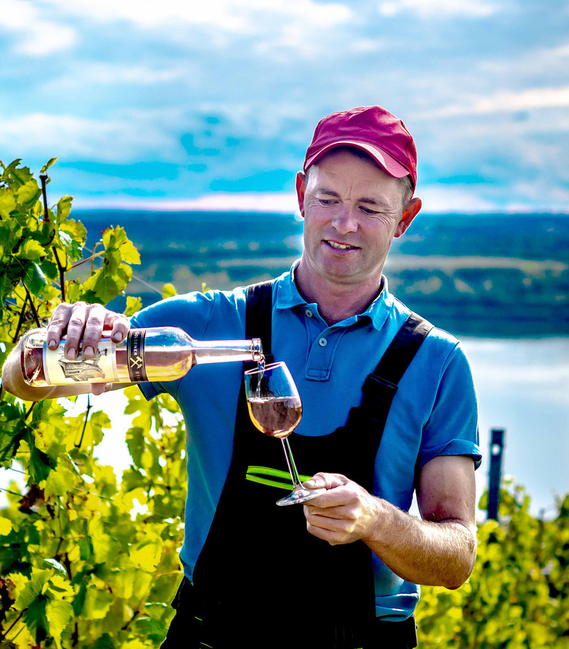 Das Bild zeigt Lars Reifert mit Weinflasche und Glas im Weinberg.