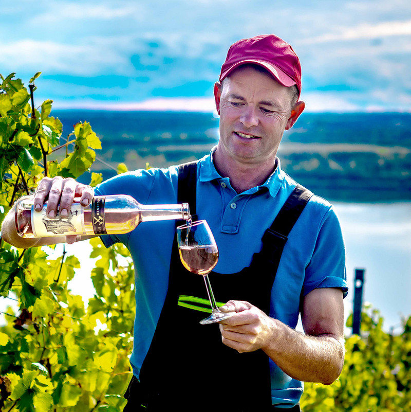 Das Bild zeigt Lars Reifert mit Weinflasche und Glas im Weinberg.