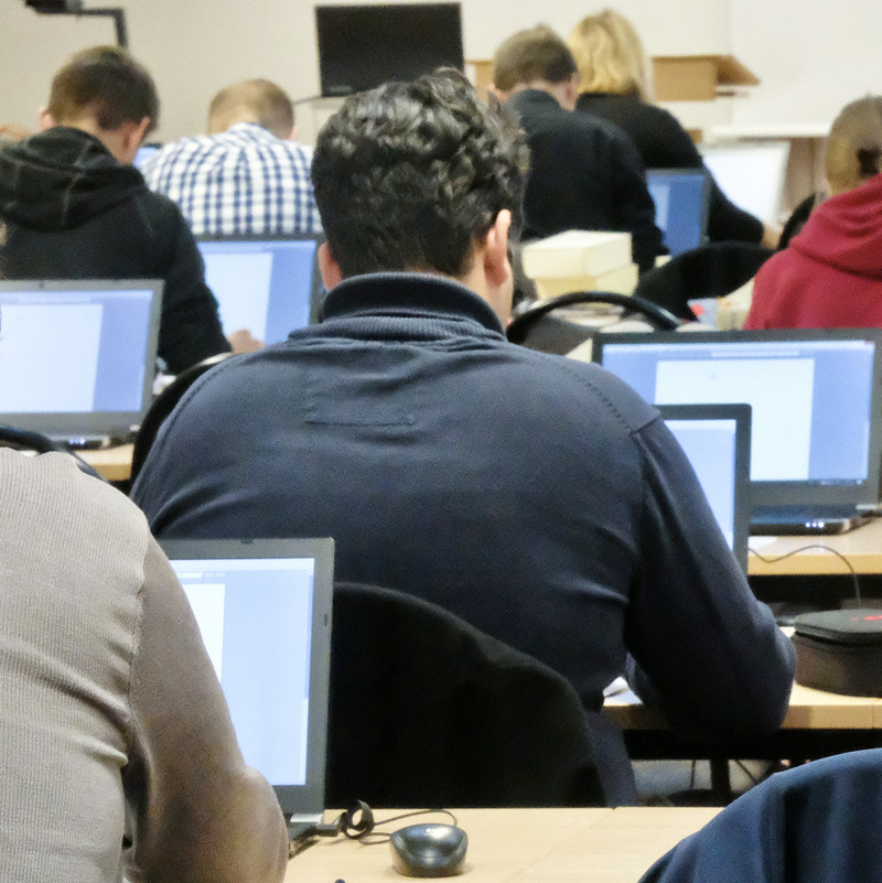 Das Bild zeigt Studierende, die an ihren Laptops das Staatsexamen ablegen. 